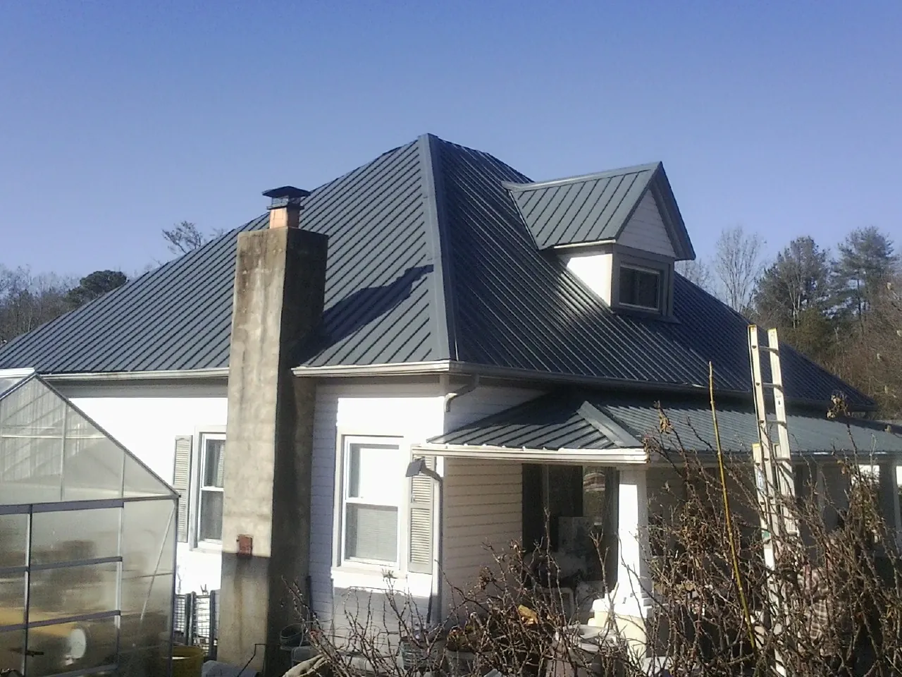Dark blue standing seam metal roof on a white farmhouse with dormer — Slate & Tile Roof Repair by Roofing Brothers in Kalispell