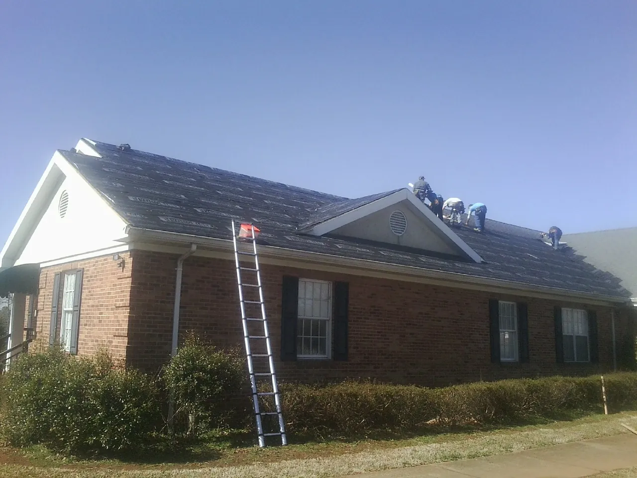 Crew tearing shingles off a brick ranch roof with a ladder set — Metal Roof Repair work by our crew in Kalispell