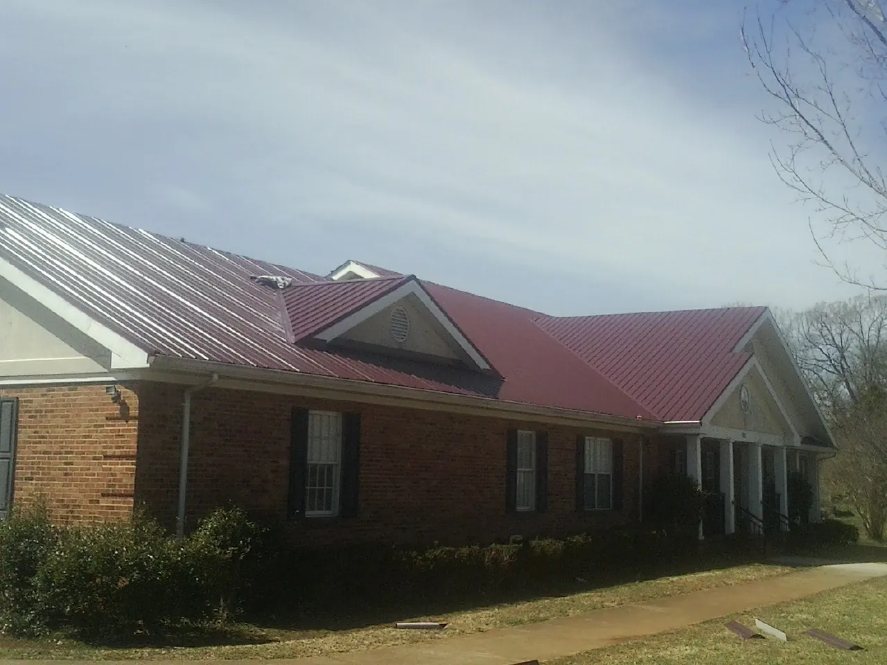 Red metal roof with gabled entries on a long brick building, from a Hail Damage Roof Repair job in Kalispell