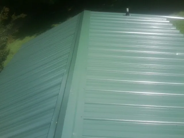 New green metal panels meeting at the ridge of a roof — Flat Roof Repair work by our crew in Kalispell