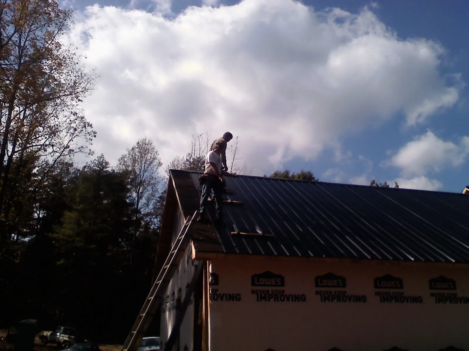 Roofer fastening dark metal panels high against a cloudy sky, from a Roof Inspection job in Kalispell