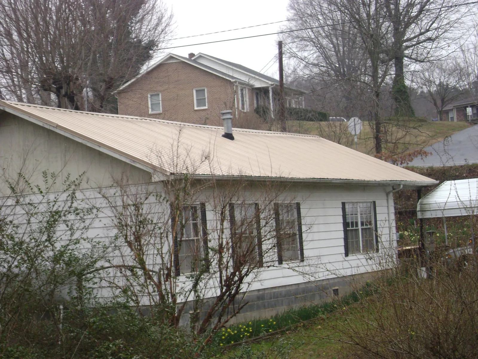 Tan metal roof on a white sided house set into a hillside — Commercial Roofing by Roofing Brothers in Kalispell